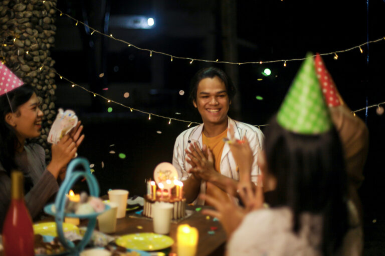 Happy family sitting around a table at an outdoor birthday celebration. Kids have party hats on.