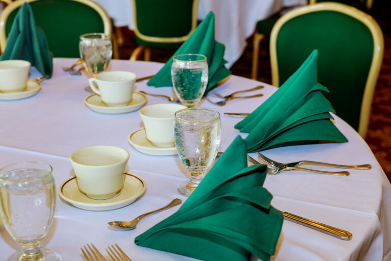 A table set with fine china and green folded napkins on top of a white table cloth.